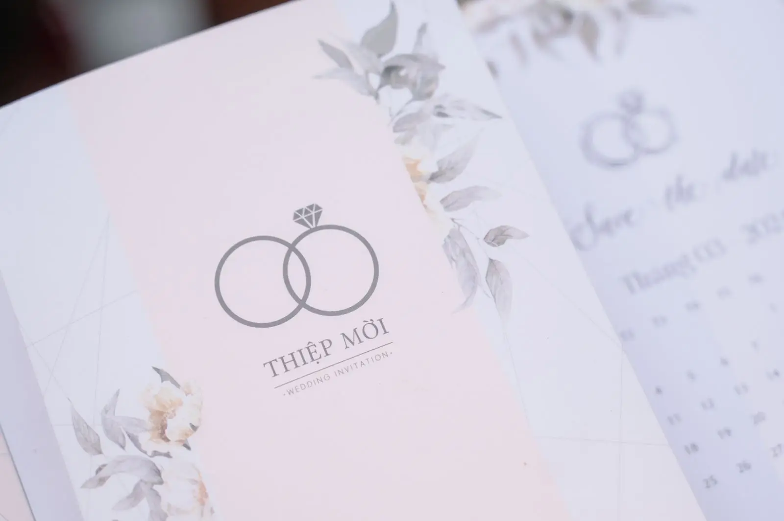 Invitație cu două verigheți desenate pe o bandă roz, ornamente florale și un calendar în fundal